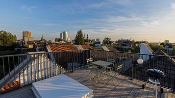 A rooftop terrace with a view of the city skyline, featuring a grill and outdoor seating.