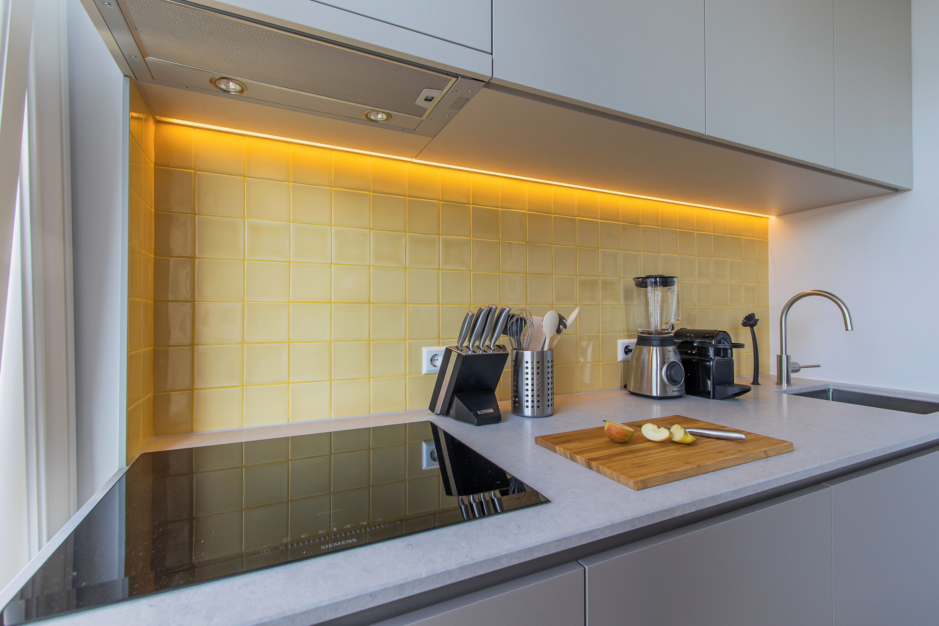 A modern kitchen with a built-in induction cooktop, a blender, and a wooden cutting board with apple slices.