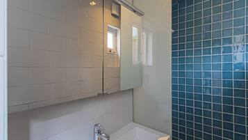 A bathroom with white tiles, a mirror, a sink, and a shower area with blue tiles.