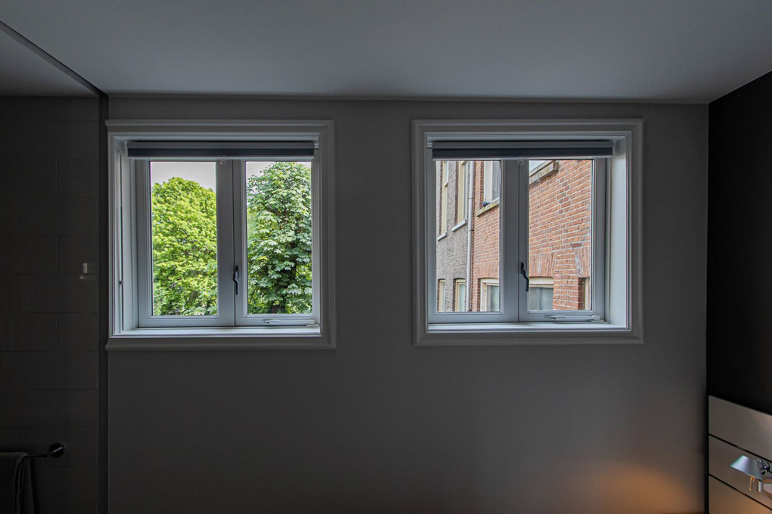 A room with two windows, one with a view of trees and the other with a view of buildings.