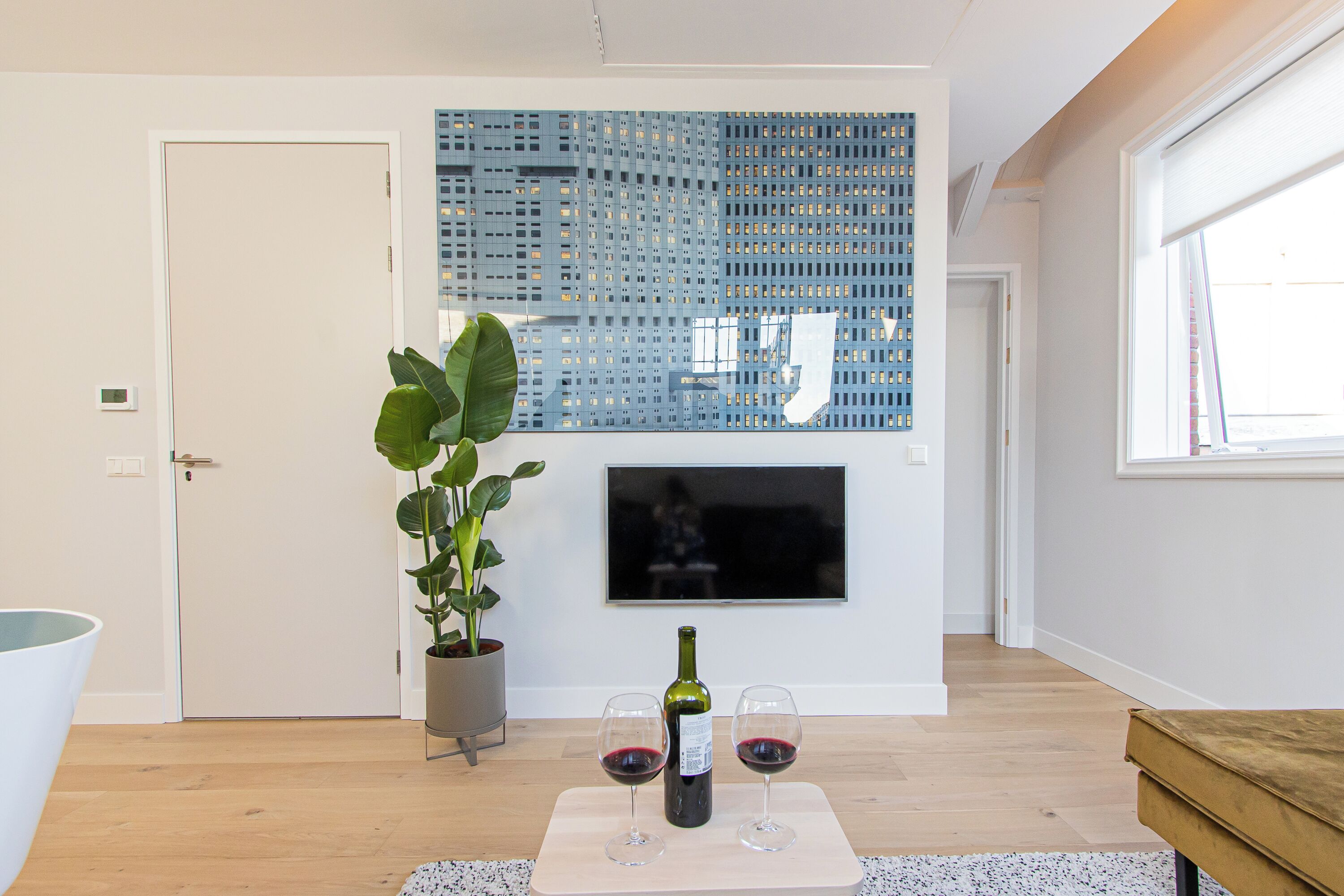 Een moderne woonkamer met een groot blauw decoratief paneel, een potplant, een fles wijn en twee wijnglazen op een tafel.