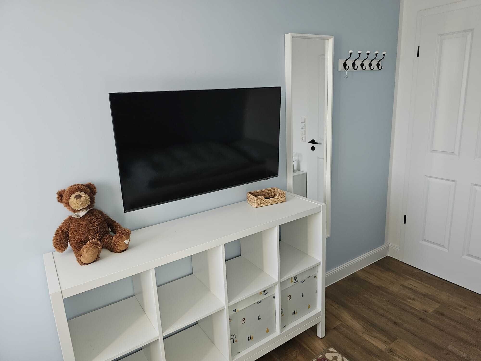 Ein Zimmer mit einer weißen Unterhaltungseinheit, die einen Flachbildfernseher und ein Stofftier beherbergt.