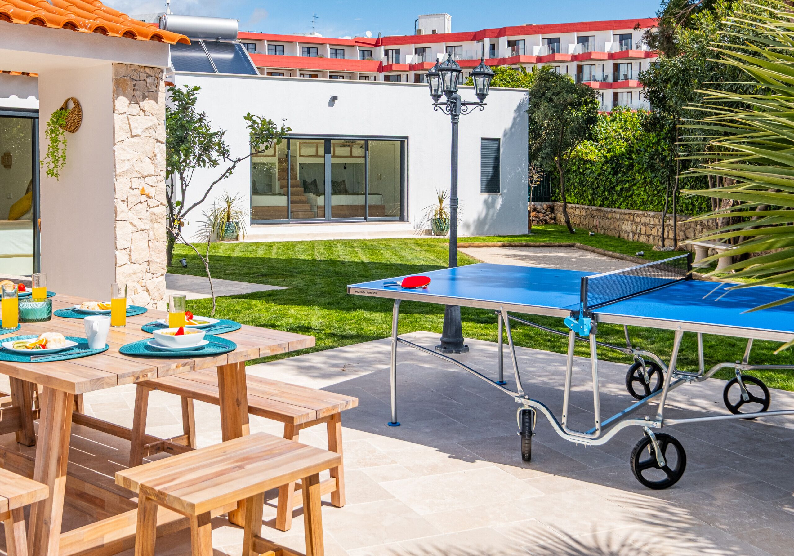 An outdoor dining area with a ping pong table, wooden benches, and a stone wall.