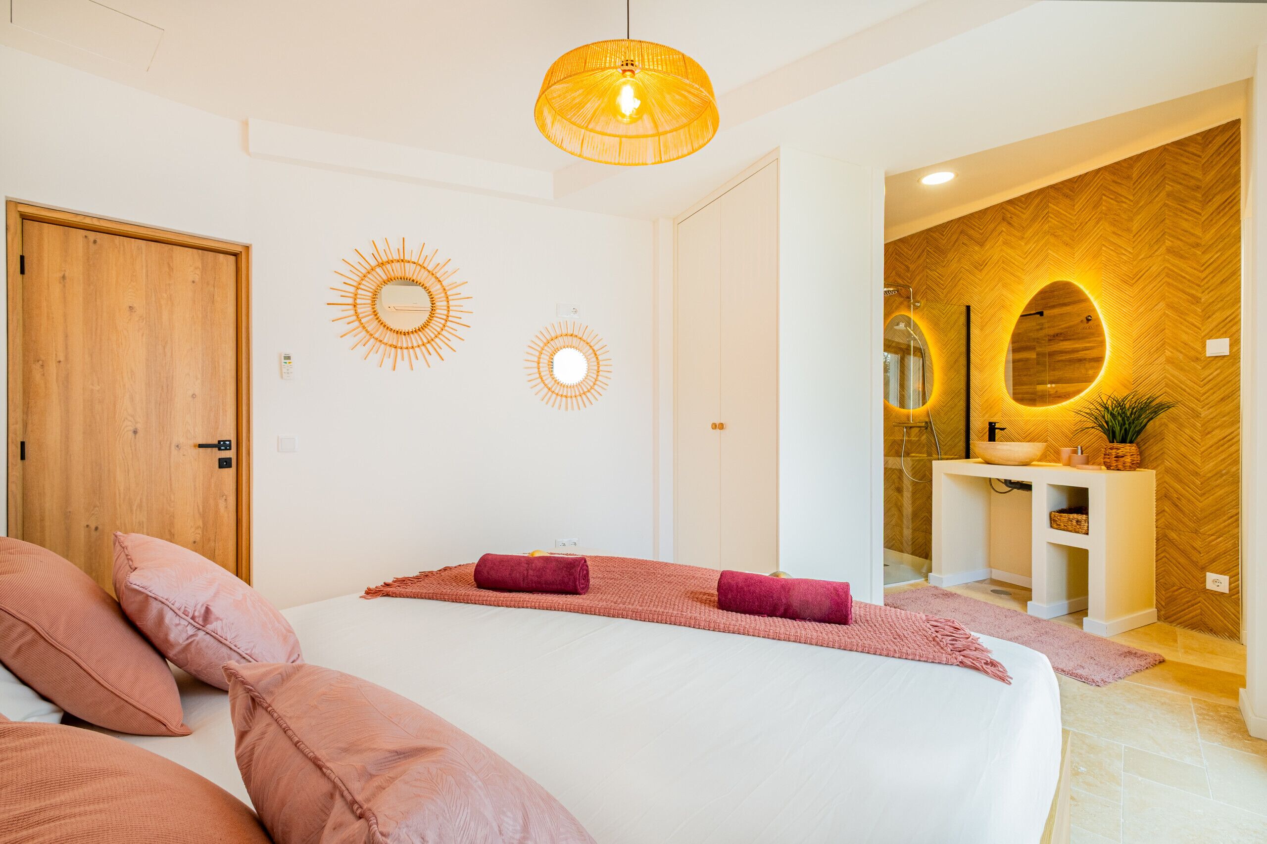 A modern bedroom with a large bed, a wooden door, and a bathroom with a herringbone-patterned wall and a round mirror.