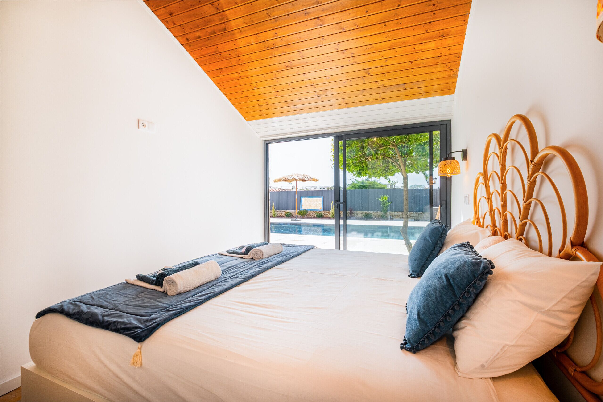 A bedroom with a large bed, wooden ceiling, and a view of an outdoor swimming pool.