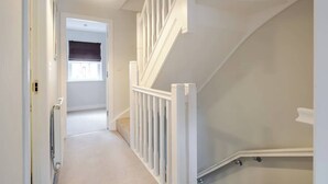 A hallway with a white railing, a radiator, and a door leading to another room. - Spacious 4 Bed Home With 2 Bathrooms & Parking (Bedford)