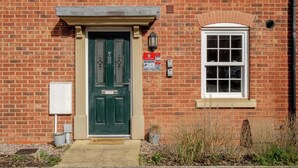 Un bâtiment en briques avec une porte verte, une fenêtre et une enseigne rouge.