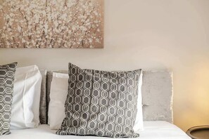 A bed with patterned pillows and a textured wall art piece above it.