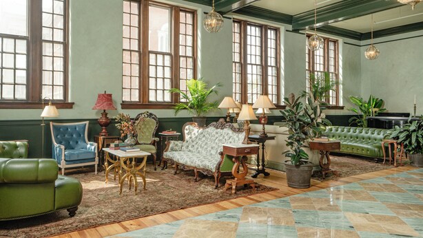 A spacious room with large windows, green upholstered sofas, a patterned rug, and classic furniture. - The Aldenberg Hotel (Versailles)