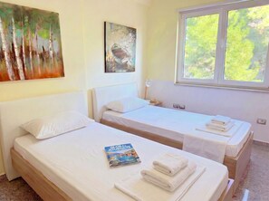 Habitación de hotel con dos camas, un cuadro en la pared, una ventana con vista a árboles y un libro titulado 'Global Journeys' sobre una de las camas.