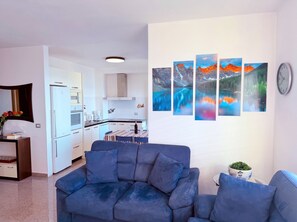 Una sala de estar con un sofá azul, un comedor con una mesa y una cocina al fondo.