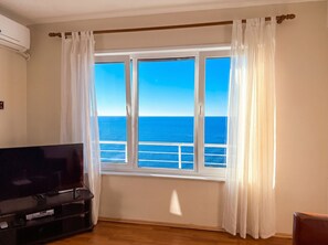 Ein Zimmer mit großem Fenster, Flachbildfernseher und Holzboden.
