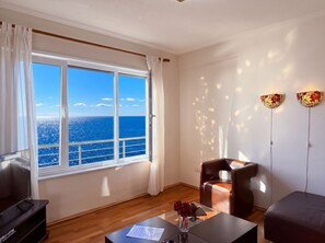 A room with a large window, a sofa, a coffee table with a vase, and a wall-mounted lamp.