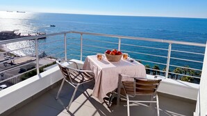 A balcony with a table set for two, overlooking a clear blue sea.