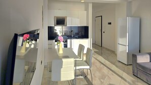 Una cocina moderna con armarios blancos, una zona de comedor con mesa y sillas, y un refrigerador.