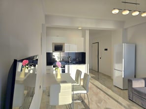 Une cuisine moderne avec des meubles blancs, un coin repas comprenant une table et des chaises, et un réfrigérateur.