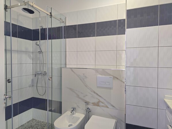 A modern bathroom with a glass-enclosed shower, a bidet, and a marble wall.