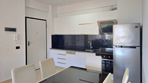 Ett modernt kök med vita skåp, en svart bänkskiva, ett kylskåp i rostfritt stål och ett matbord i glas med tillhörande stolar.