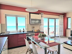 A kitchen with a view of the sea, a dining area with a glass table, and a TV mounted above the stove.