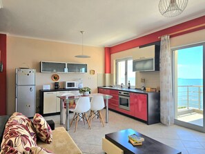 Une cuisine moderne avec des meubles de rangement rouges et blancs, un coin repas doté d’une table en verre et un canapé agrémenté de coussins à motifs.