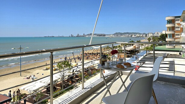 A balcony with a table set for breakfast, overlooking a beach and cityscape. - Dream View Apartment Durres 119 (Durres)