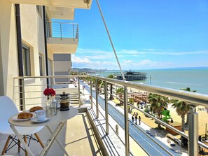 Un balcón con una mesa dispuesta para el desayuno, con vista a una playa y al mar.