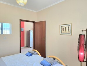 A bedroom with a bed, a door, a mirror, a framed picture, and a red lamp.