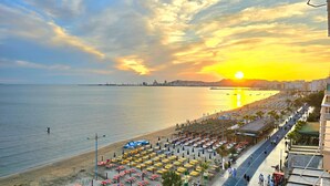 A beach with rows of umbrellas and sun loungers, a promenade with people walking, and a sunset over the water. - Dream View Apartment Durres 119 (Durres)