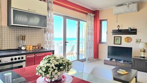 A modern kitchen with a Zanker stove, a glass dining table with a white flower centerpiece, a TV, and a balcony with a view of the sea. - Dream View Apartment Durres 119 (Durres)