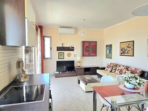A modern living room with a sofa, a TV, and a dining area with a glass table.