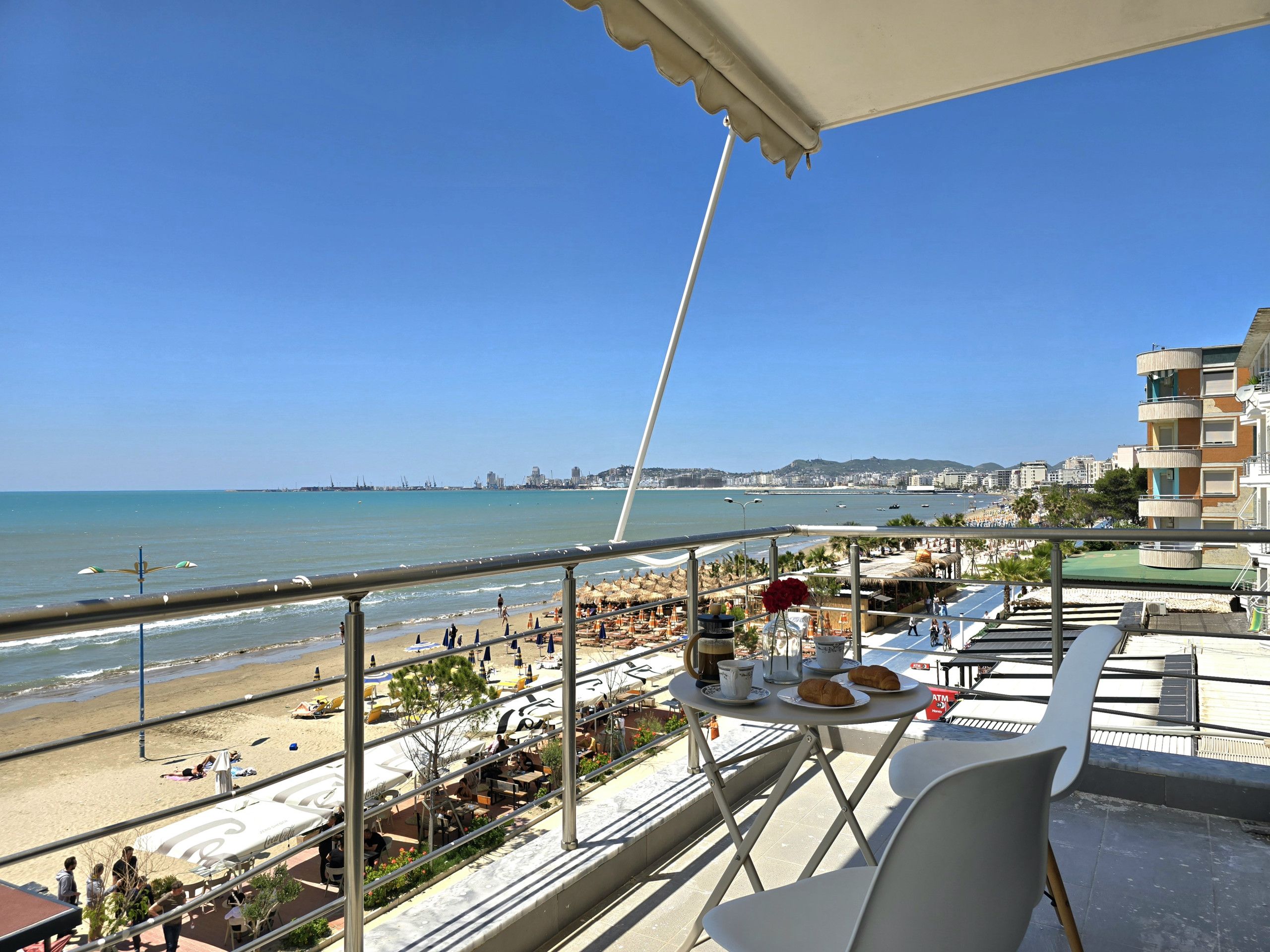 A balcony with a table set for breakfast, overlooking a beach and cityscape.