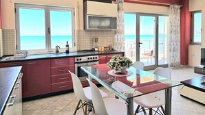 A kitchen with a view of the sea, a dining area with a glass table, and a TV mounted above the stove. - Dream View Apartment Durres 119 (Durres)