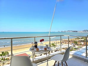 Un balcón con una mesa para dos, con vistas a la playa y al paisaje urbano.