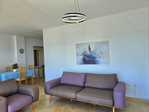 A modern living room with a grey sofa, two armchairs, a dining table with chairs, and a contemporary painting on the wall.