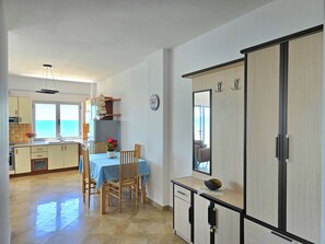 A compact kitchen with a dining area, a large mirror, and a view of the sea through the windows.