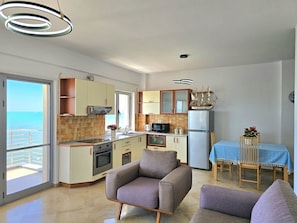 A modern kitchen with a view of the sea, a dining area with a table and chairs, and a living room with sofas.