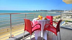 Une table recouverte d’une nappe blanche, avec des chaises rouges, et une vue sur la plage et l’océan.