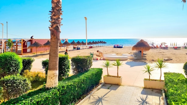 Une plage bordée de palmiers, avec des parasols et un ciel dégagé.