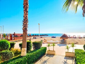 Ein Strand mit Palmen, Sonnenschirmen und blauem Himmel.