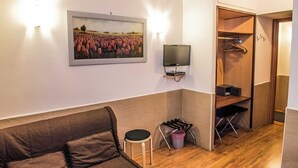Ein Zimmer mit einem braunen Sofa, einem kleinen Hocker, einem Fernseher, einem Holzschrank und einem Bilderrahmen mit Tulpen an der Wand.