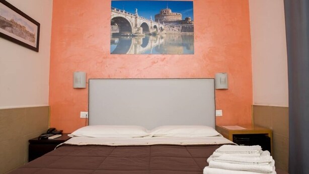 Ein Hotelzimmer mit einem großen Bett, einem Kopfteil, zwei Nachttischen, einem Fenster mit Vorhängen und einem gerahmten Bild an der Wand.