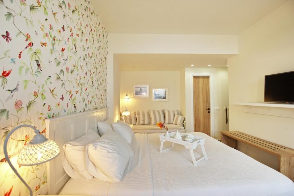 Una camera d'albergo con un letto, un comodino con una lampada, un divano e una televisione appesa al muro.