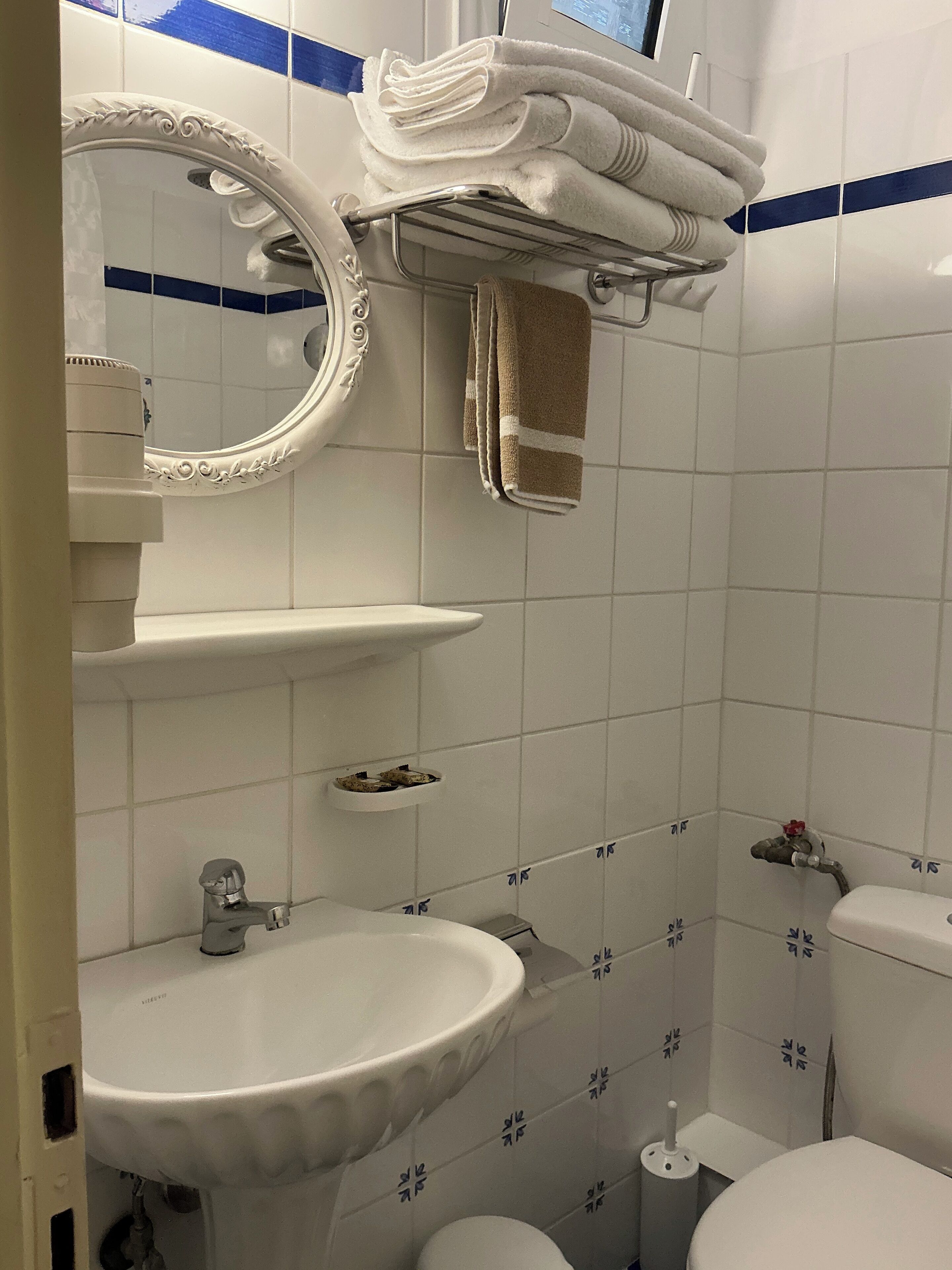 Ein Badezimmer mit weißem Waschbecken, Toilette, einem Spiegel mit aufwendigem Rahmen und einem Handtuchhalter mit gefalteten Handtüchern.