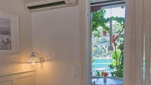 A bedroom with a bed, a wall-mounted air conditioner, a bedside lamp, and a view of a balcony with a table and chairs. - Liadromia Hotel (Alonissos)