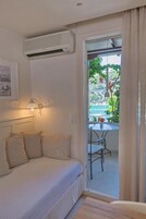Un dormitorio con una cama, aire acondicionado instalado en la pared, una lámpara de noche y vistas a un balcón con mesa y sillas.