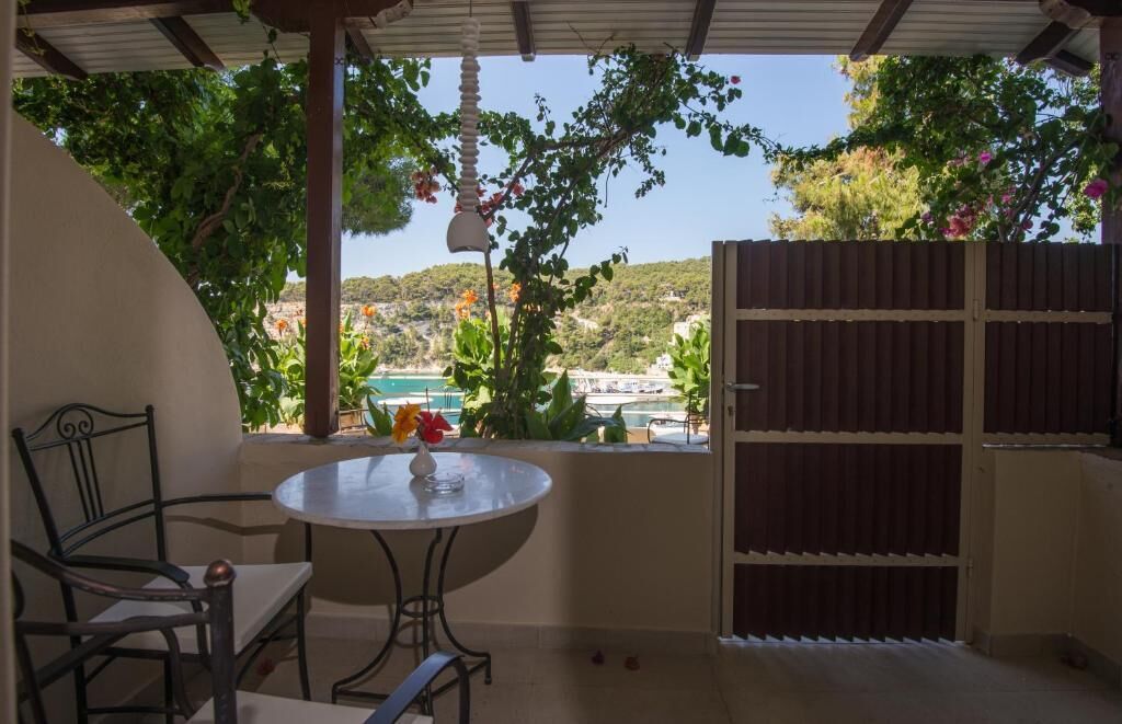 A covered patio with a table and chairs, a view of a coastal area, and a wooden gate.