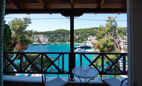 Un balcon avec vue sur une mer turquoise, des bateaux et un paysage vallonné.