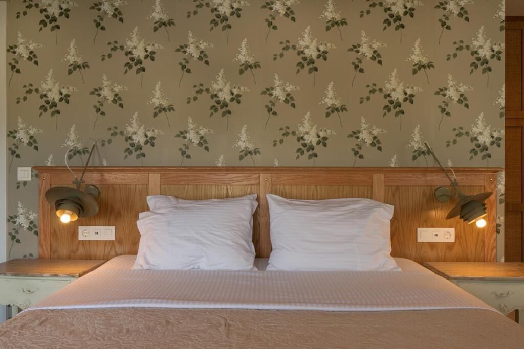 Quarto com cabeceira de madeira, duas luminárias de cabeceira e um padrão floral no papel de parede.