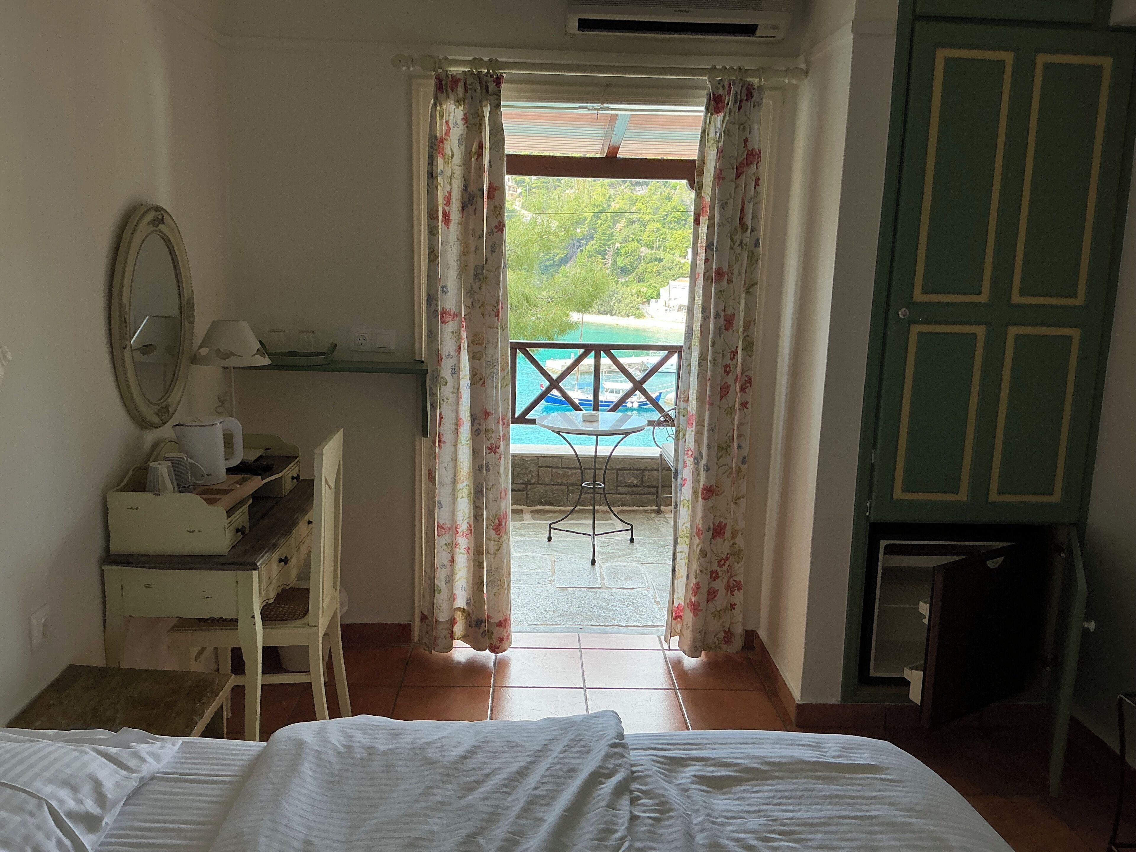 Une chambre d’hôtel avec un lit, un bureau doté d’un miroir, une petite table et une vue sur une piscine et la verdure environnante.