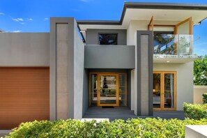A modern two-story house with a garage, a balcony, and a glass door entrance.